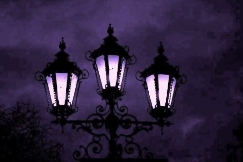 three street lamps lit up against a dark night sky with clouds in the back ground