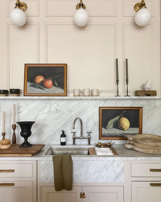 a kitchen with white cabinets and marble counter tops, two framed pictures above the sink