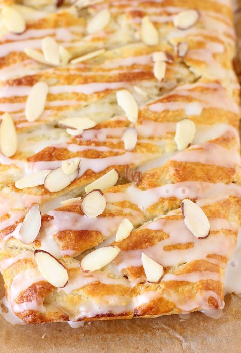 a pastry with almonds and icing sitting on top of a piece of parchment paper