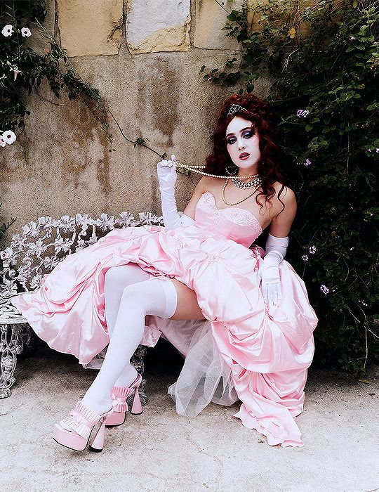 a woman in a pink dress is sitting on a bench with flowers and vines around her