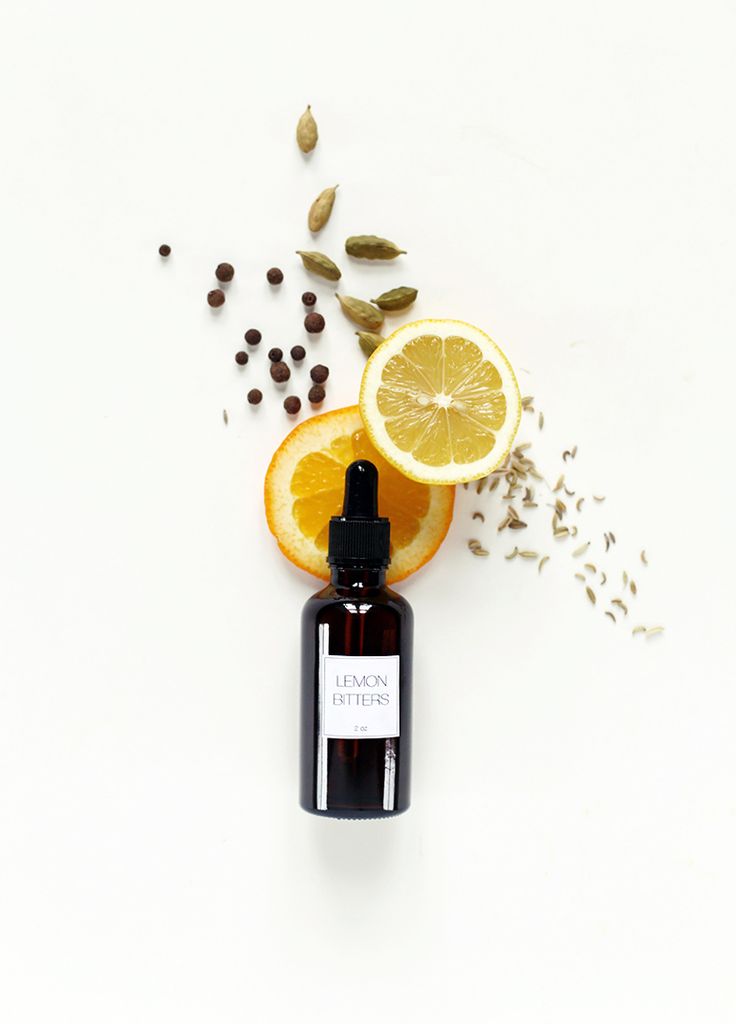 an orange slice and some seeds are next to a bottle of essential oil on a white surface