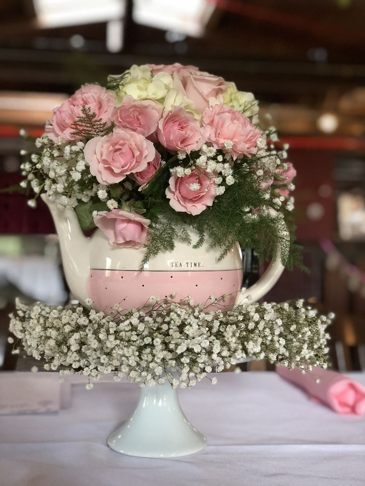 a white tea pot with pink flowers and baby's breath in it sitting on top of a table