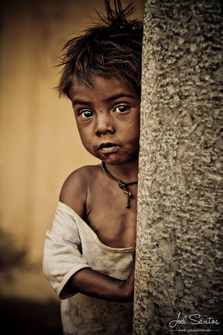 a young boy is peeking out from behind a tree