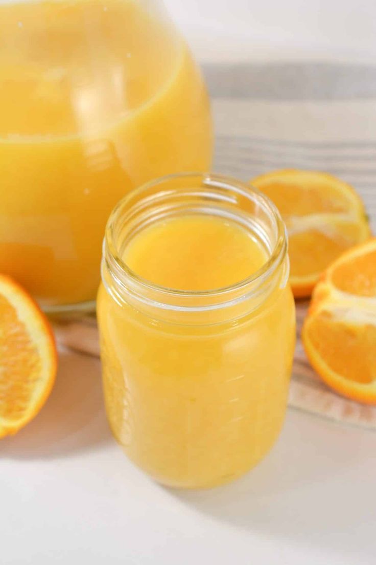 two jars filled with orange juice next to sliced oranges on a white tablecloth