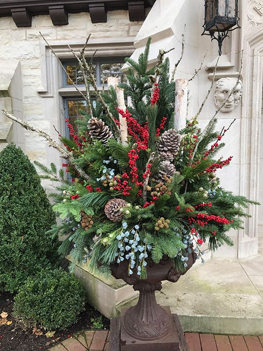 a planter filled with pine cones, berries and evergreens in front of a house