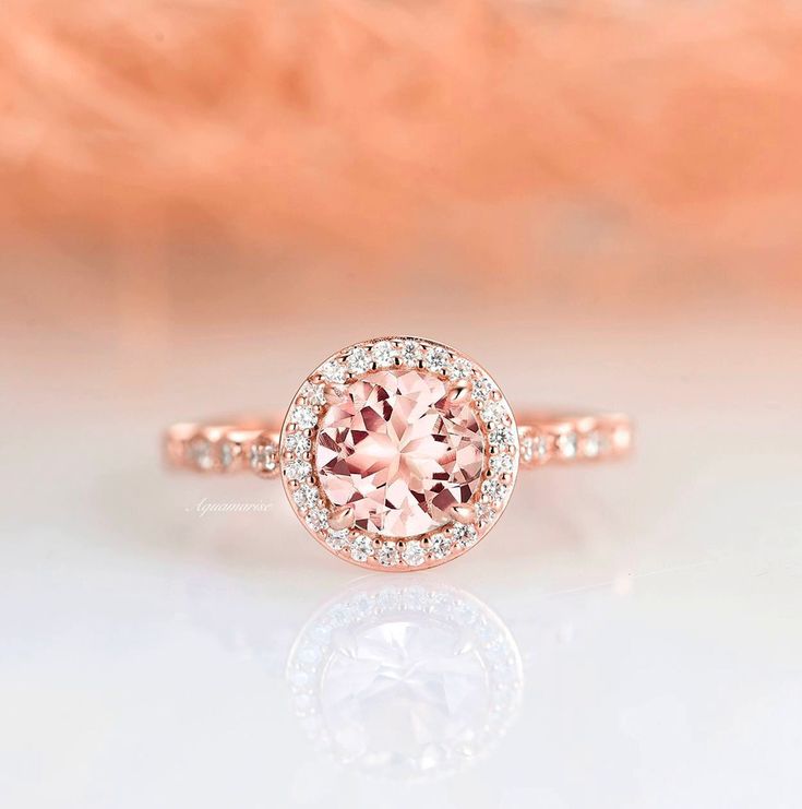 a pink diamond ring on top of a white surface with an orange flower in the background