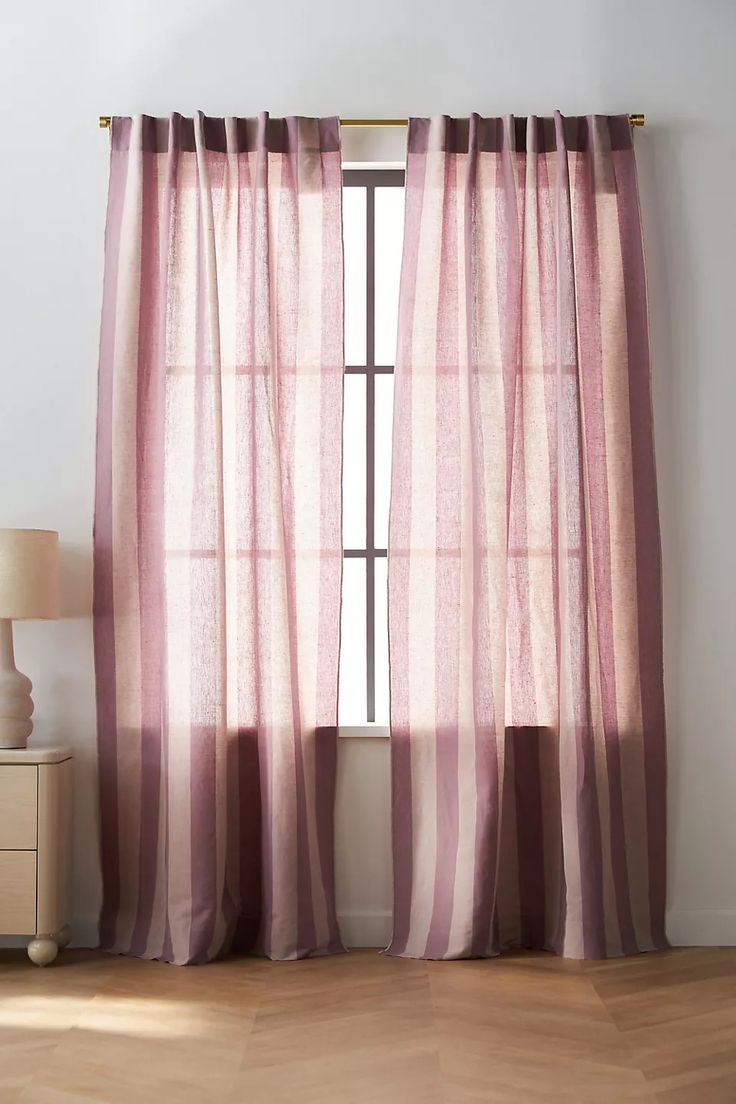 a window with pink curtains in front of it and a lamp on the side table