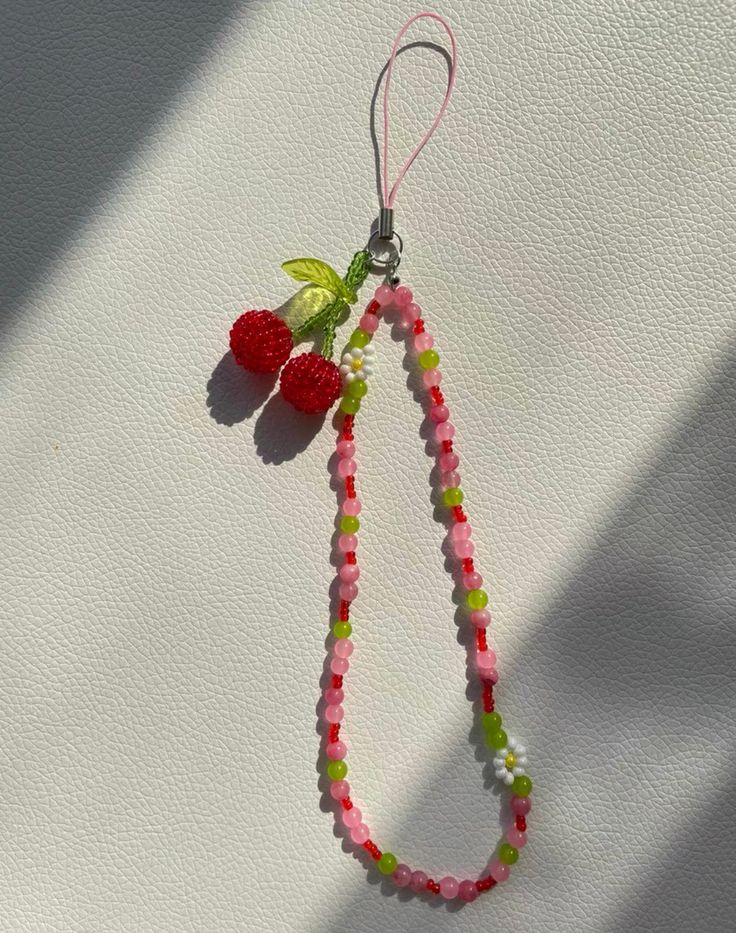 a beaded necklace with two cherries hanging from it's end on a white surface