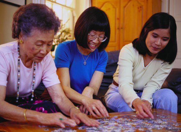 three women sitting on the floor playing with a puzzle piece in front of them while another woman looks at it