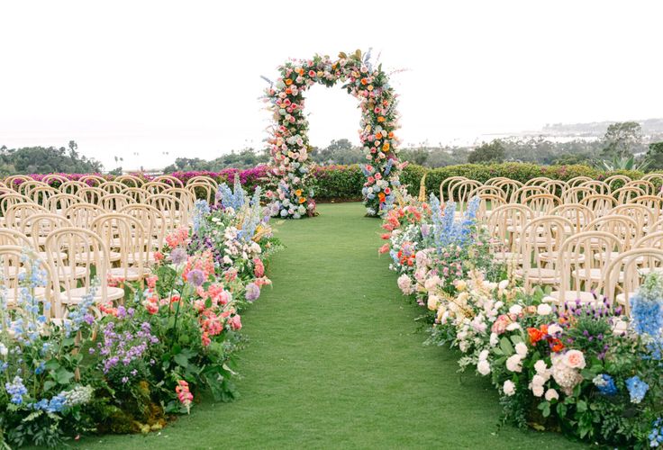 an outdoor ceremony setup with rows of chairs and flowers on the grass in front of them