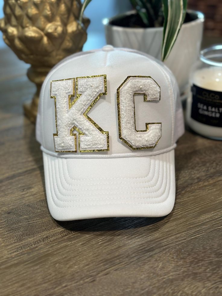 a white hat with the letter kc on it sitting next to a potted plant