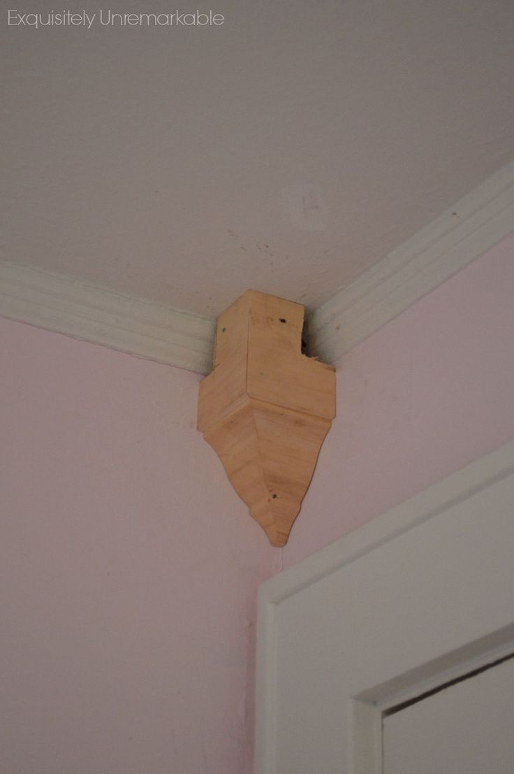 a wooden clock mounted to the side of a pink wall in a room with white trim