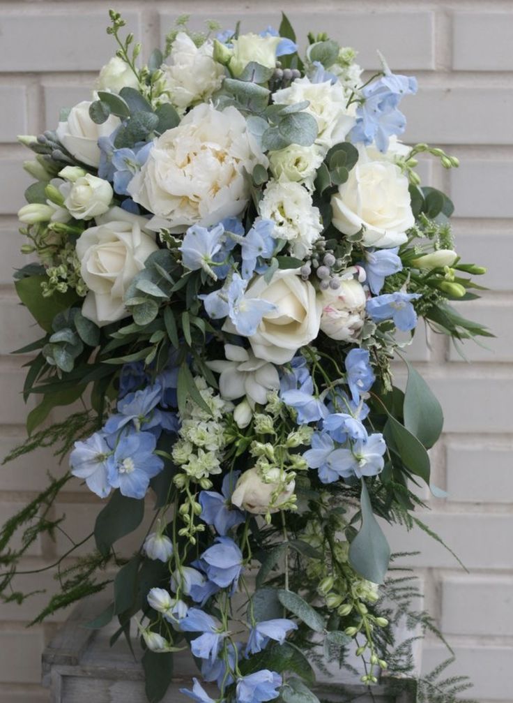 a bouquet of white and blue flowers in front of a brick wall with greenery