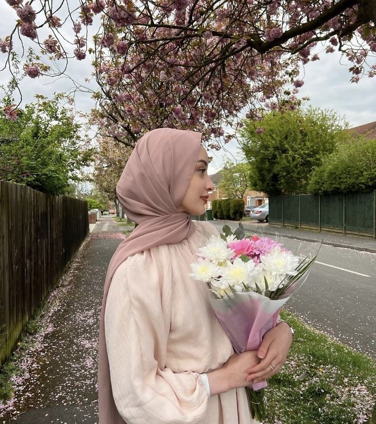 a woman in a hijab holding a bouquet of flowers on the side of a road