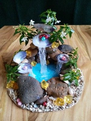 a small fountain made out of rocks and stones with plants growing on the top, sitting on a wooden table