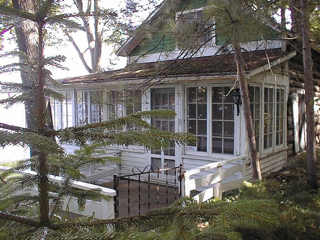 the house is surrounded by pine trees and has a porch with an open door on it