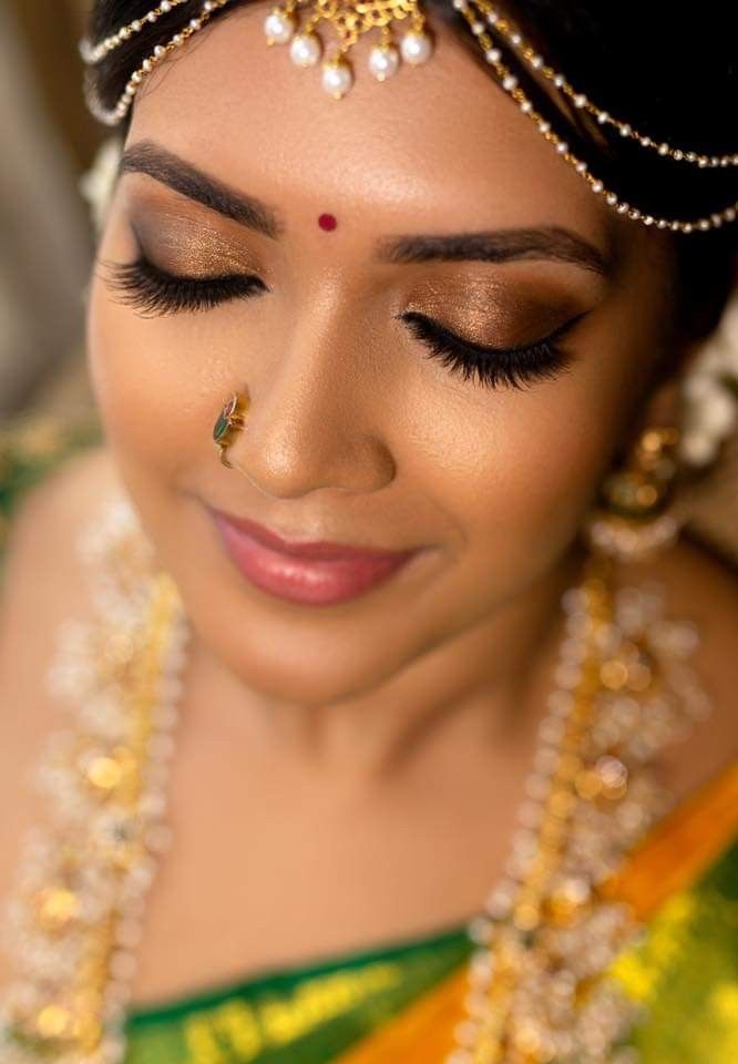 a woman in a green and gold sari with pearls on her forehead, wearing a nose ring