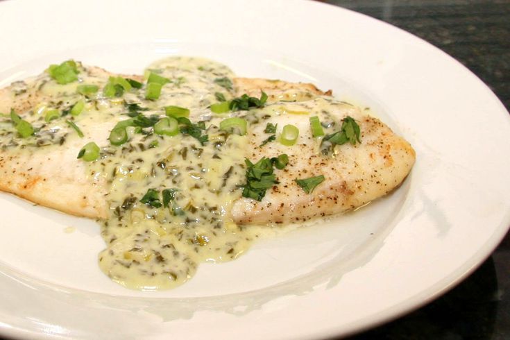 a white plate topped with fish covered in sauce and green onions on top of it