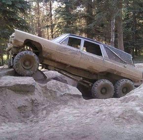 an off road vehicle is stuck in the mud on top of some rocks and trees