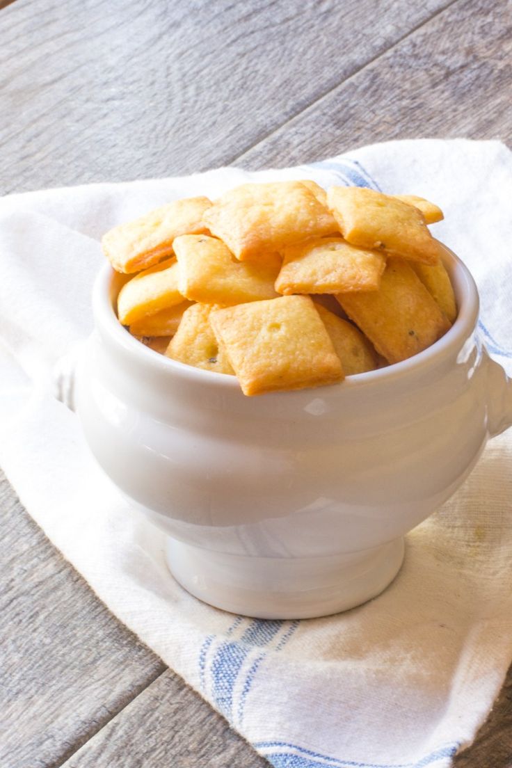 a white bowl filled with crackers sitting on top of a wooden table next to a blue and white towel