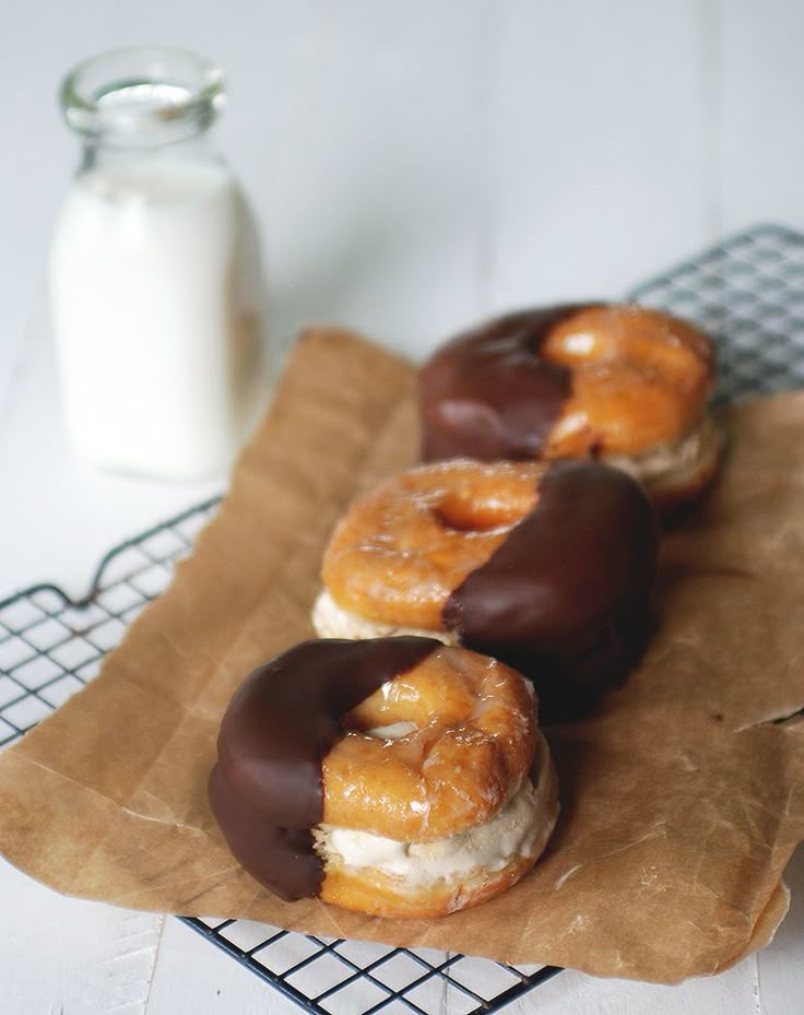 chocolate covered donuts sitting on top of a brown paper bag next to a glass of milk