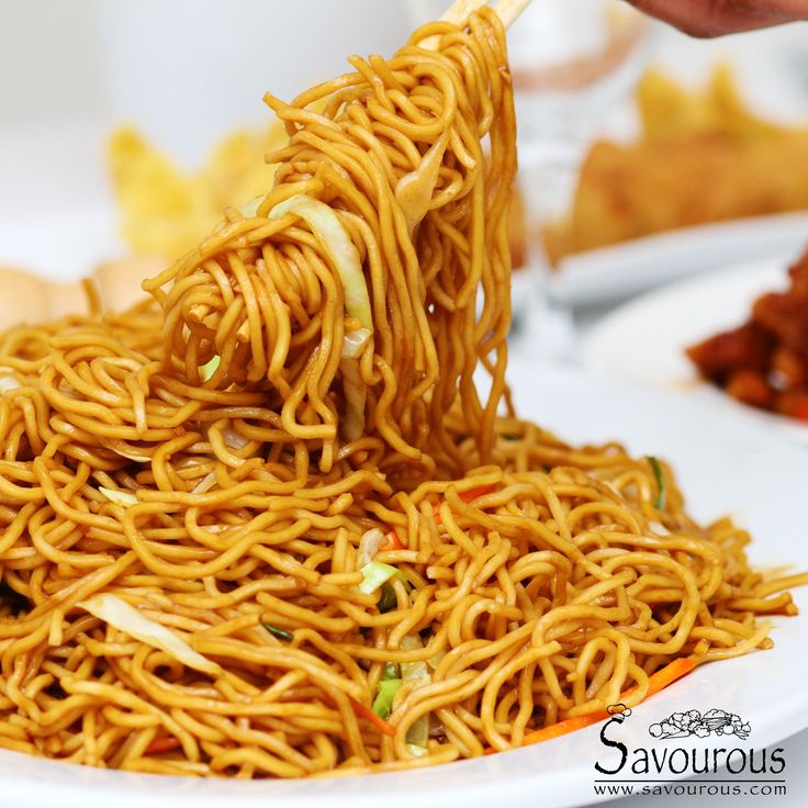 a person is holding chopsticks over noodles on a plate with other plates in the background