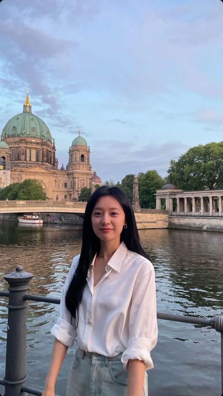 a woman standing next to the water in front of a building