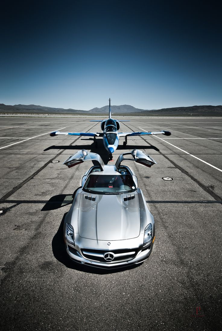 a silver sports car parked on top of an airport tarmac with two planes in the background