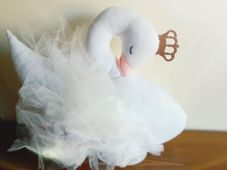 a white stuffed swan with a tiara on it's head sitting on a table