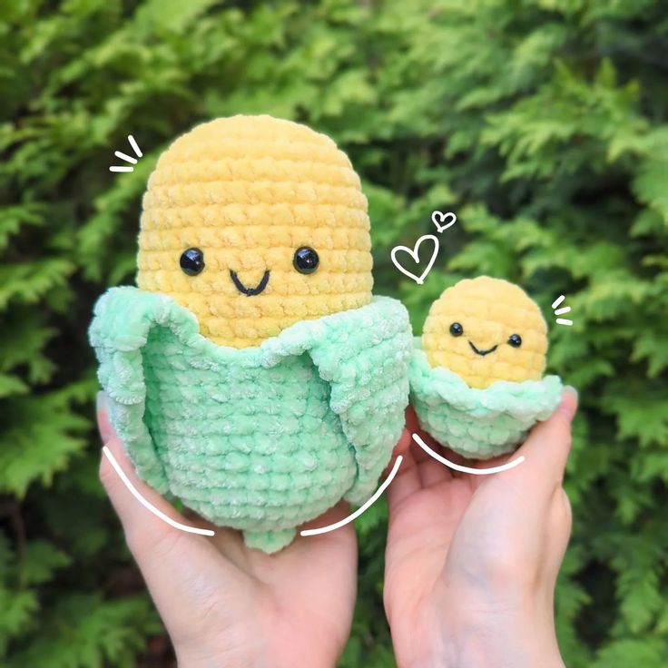 someone holding two small stuffed toys in their hands, one is yellow and the other is green