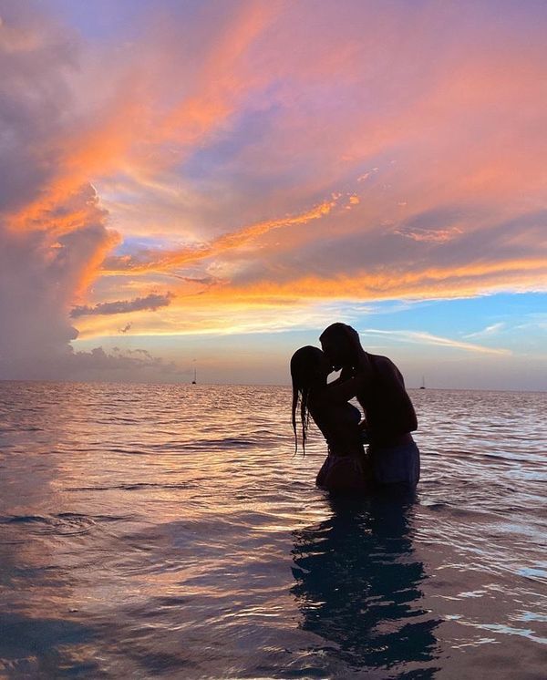 a man and woman kissing in the ocean at sunset with clouds reflecting off the water