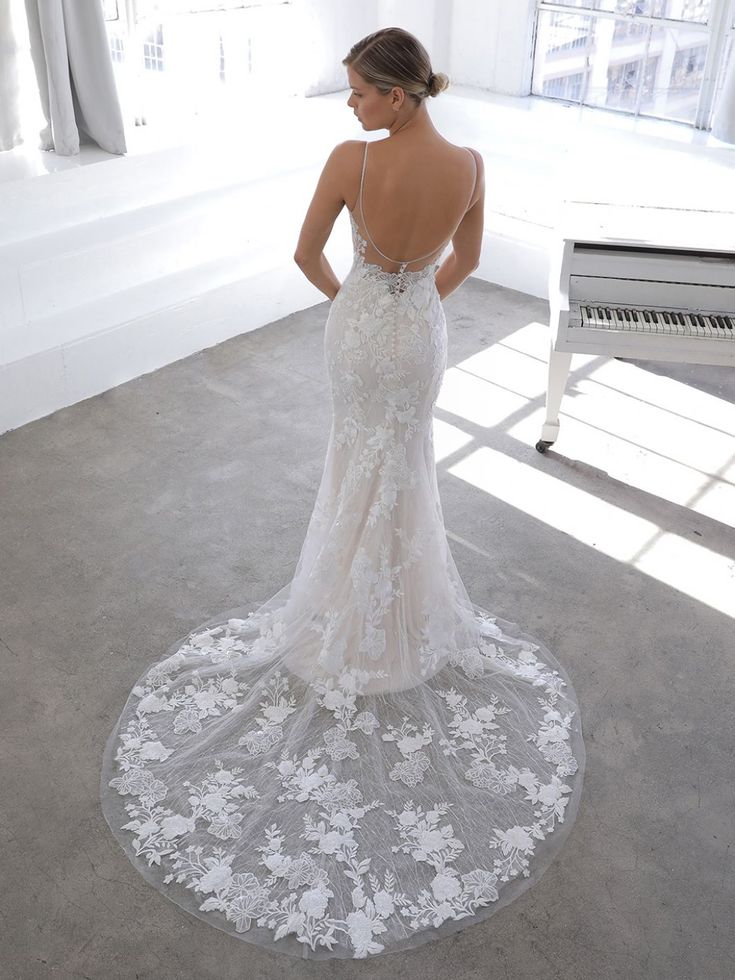 a woman standing in front of a piano wearing a wedding dress with an open back