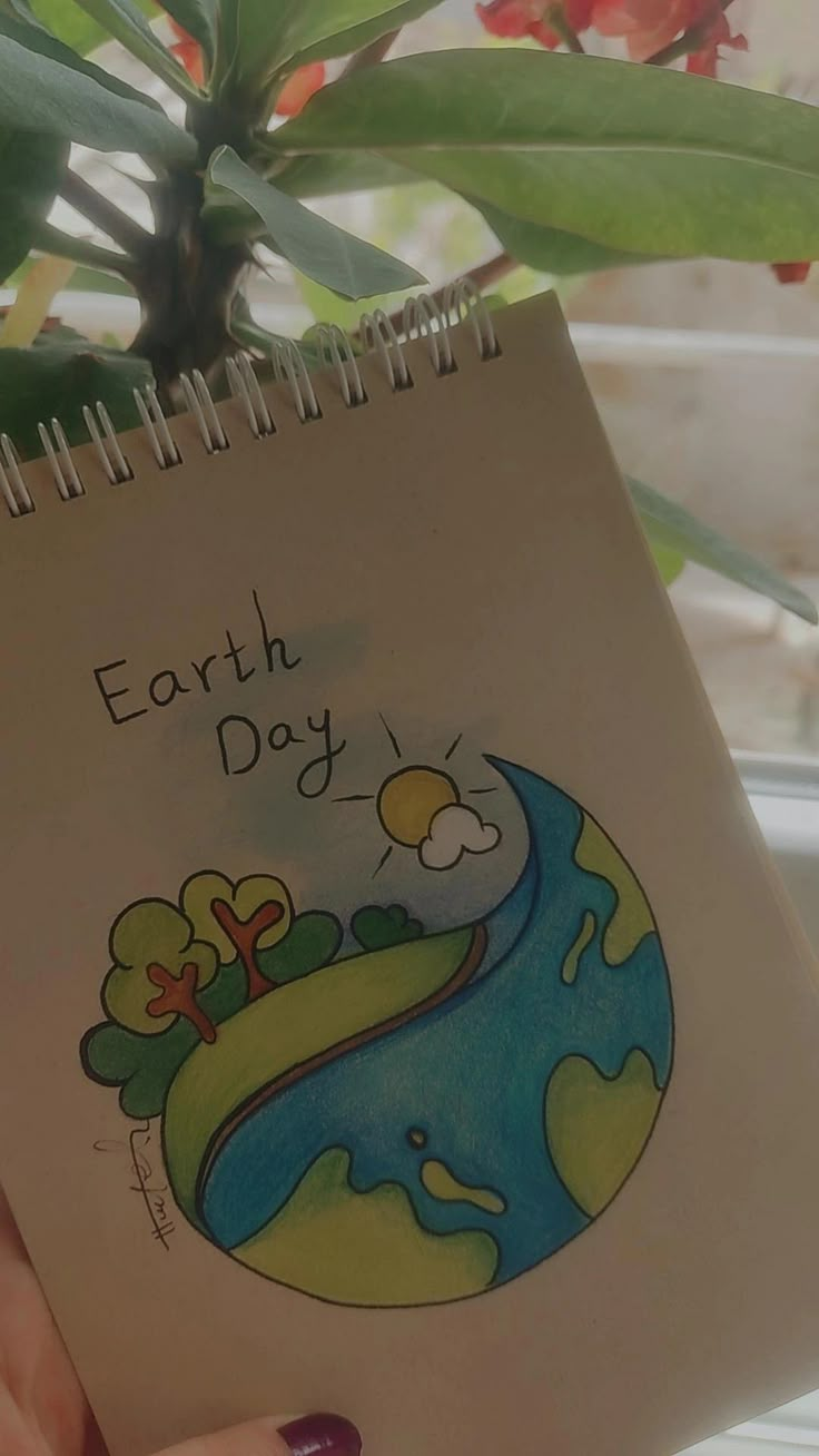 a hand holding a notebook with the earth day written on it and a plant in the background