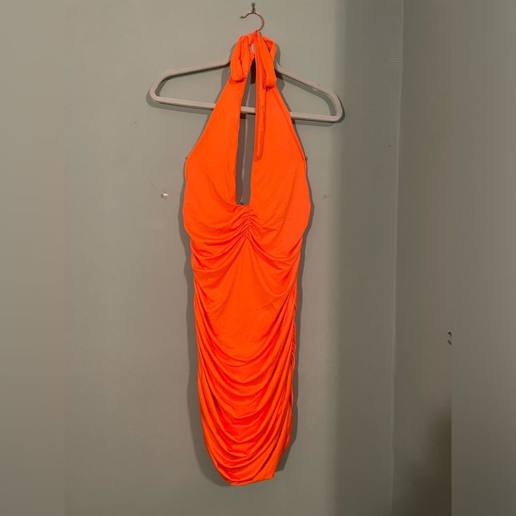 an orange dress hanging on a hanger next to a white wall in a bathroom