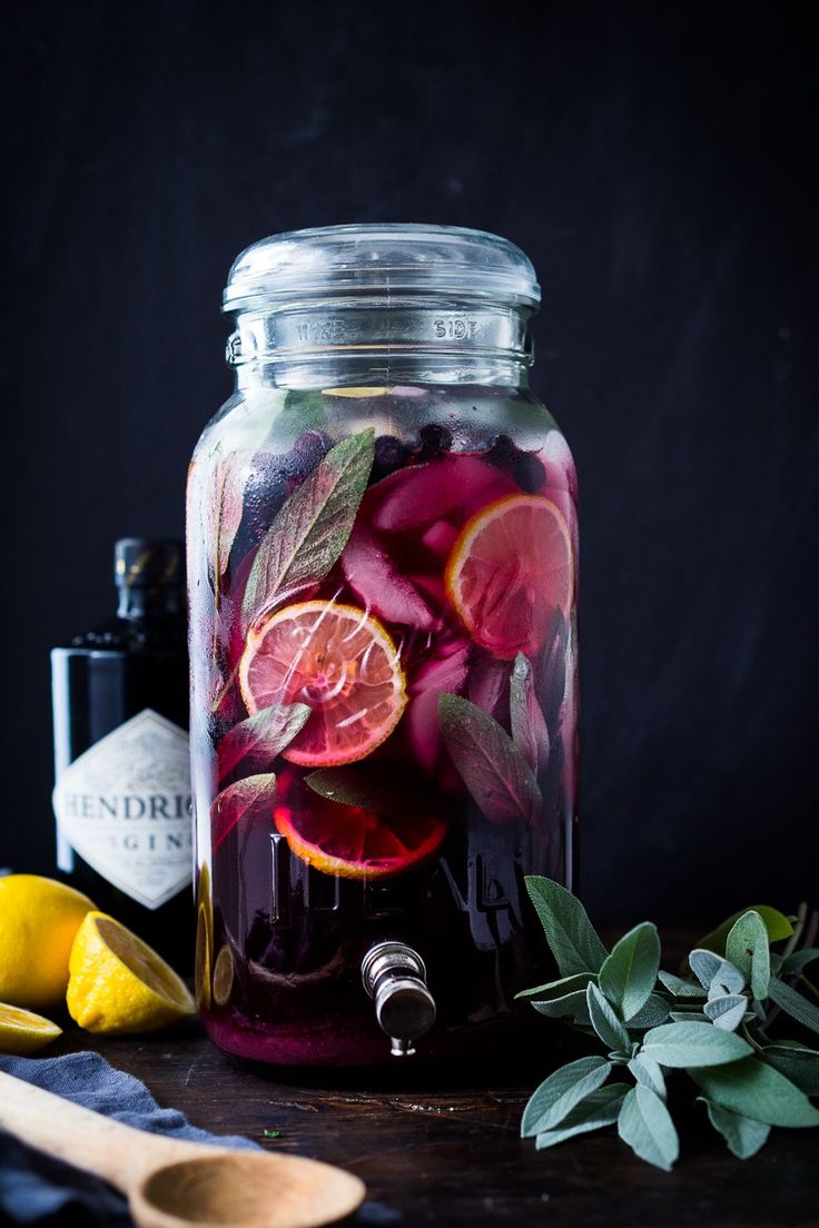 a jar filled with liquid next to lemons and herbs