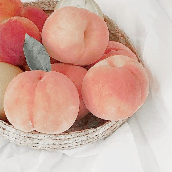 some peaches and apples in a basket on a white tablecloth with a green leaf