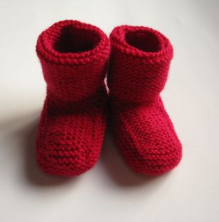 two red knitted baby booties sitting on top of a white table