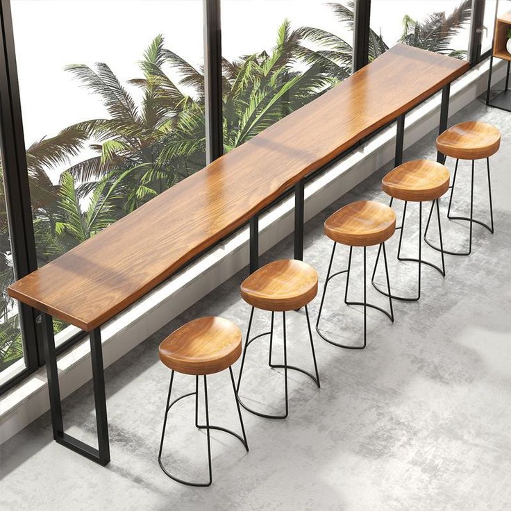 four wooden stools sitting next to each other in front of a large window with palm trees