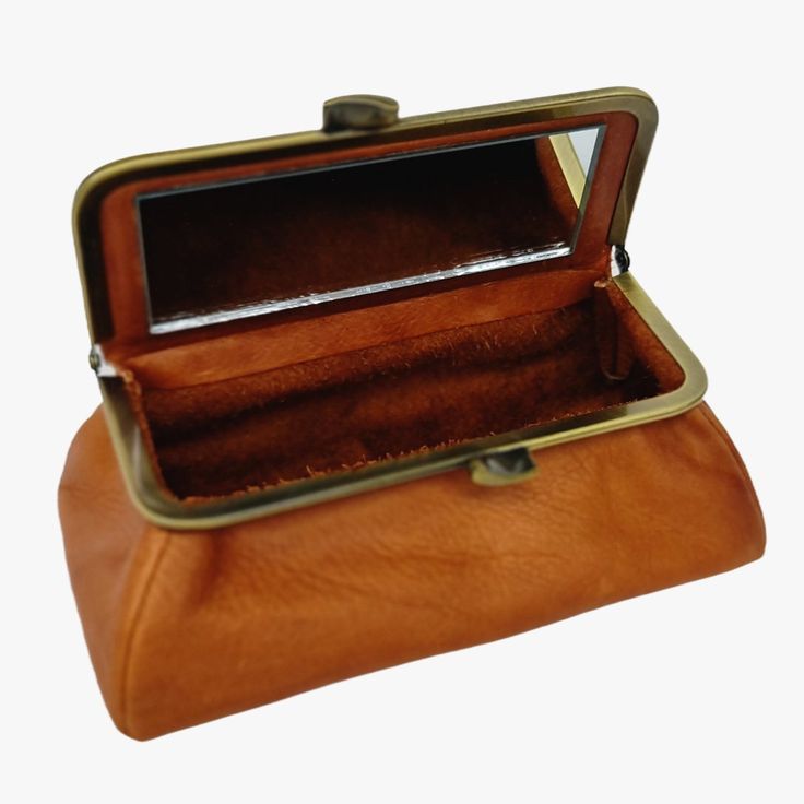 Introducing a vintage-inspired, handmade travel jewelry or cosmetic pouch crafted from high-quality Italian leather. This genuine leather pouch features a classic, timeless design that seamlessly transitions from your grandma's treasure trunk to your everyday bag.Sized perfectly to hold all your daily makeup essentials and more, this pouch is versatile and easily fits inside a purse or tote bag. Its lid features a full-size mirror with a non-distorting, clear image, making on-the-go makeup application a breeze.The pouch is secured with a gold-tone kiss-lock clasp made in the UK and is branded with a small logo plaque on the front. It comes in a rich orange color with a brushed bronze frame.Crafted entirely from a genuine Italian supple napa leather, this cosmetic pouch is meticulously hand Classic Compact Wallet For Daily Use, Classic Formal Coin Purse Pouch, Classic Rectangular Cosmetic Bag For Everyday Use, Formal Classic Coin Purse Pouch, Vintage Leather Pouch For Travel, Classic Rectangular Cosmetic Bag, Vintage Leather Pouch With Coin Pocket, Vintage Rectangular Case Bag For Everyday Use, Vintage Brown Rectangular Wallets For Daily Use