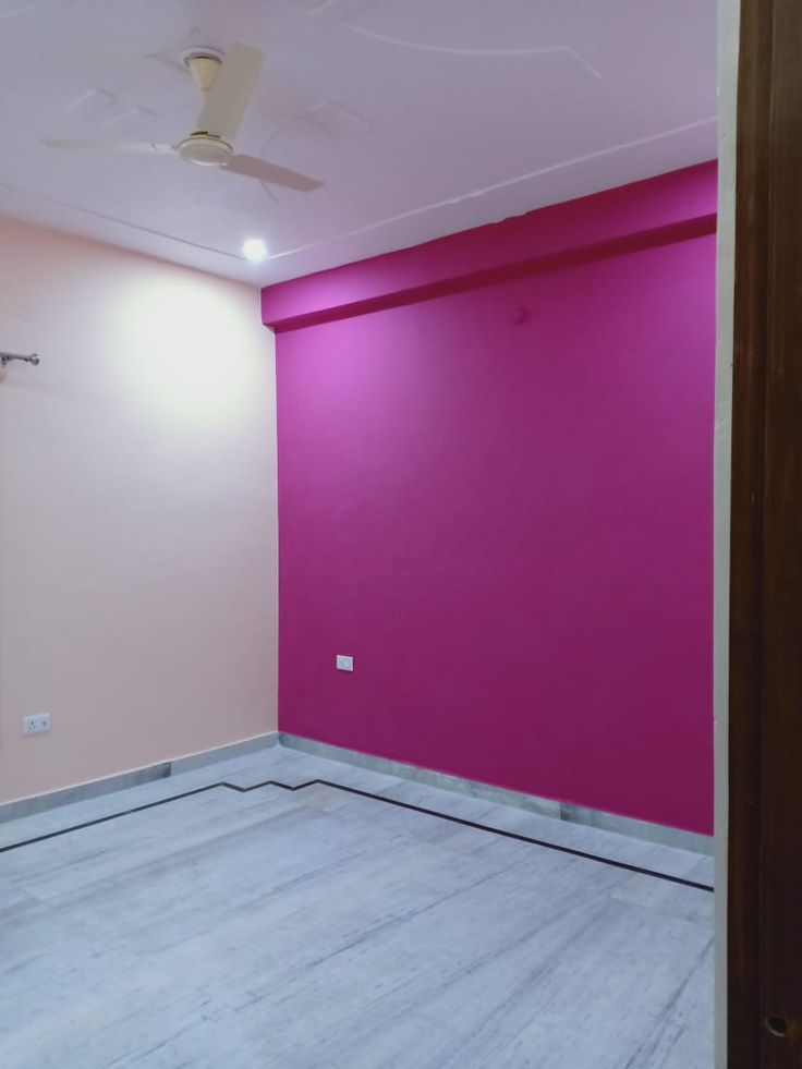 an empty room with pink walls and ceiling fan in the corner on the far wall