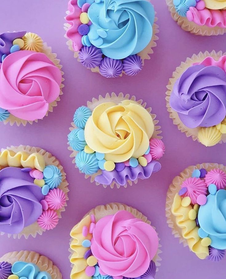 cupcakes with colorful frosting are arranged on a purple surface