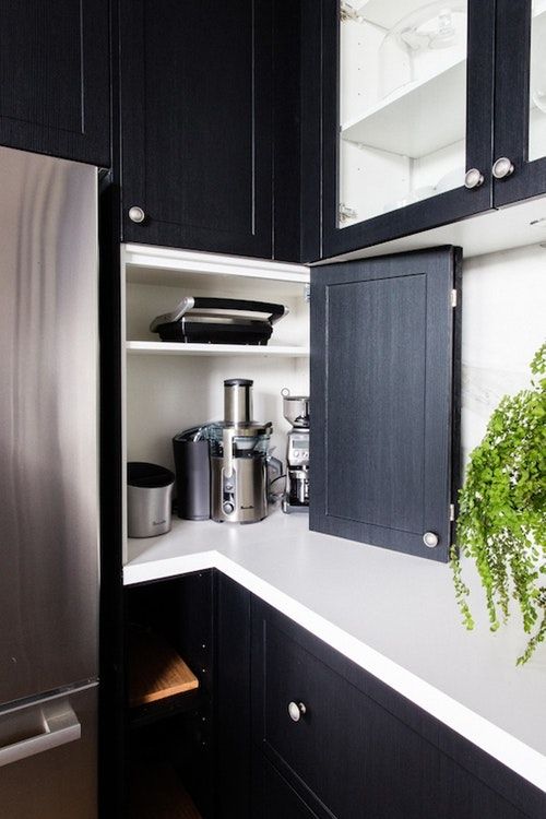 a kitchen with black cabinets and white counter tops, an open refrigerator freezer is in the corner