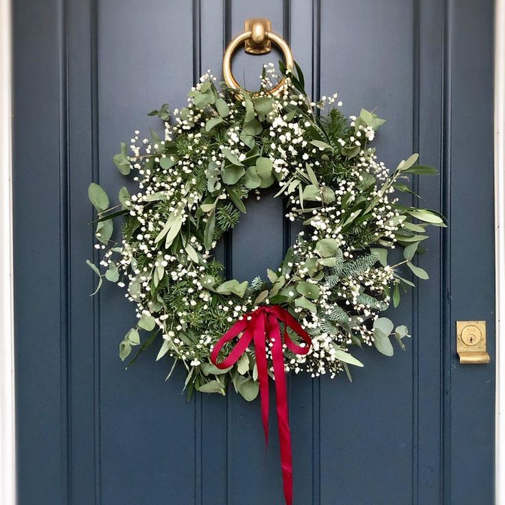 a wreath hanging on the front door of a house with red ribbon and white baby's breath