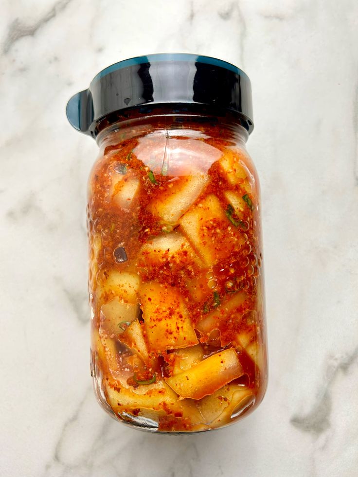 a glass jar filled with food sitting on top of a marble counter next to a blue lid