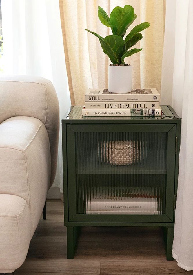 a green side table with books and a potted plant sitting on top of it