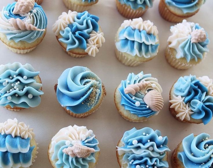 cupcakes with blue frosting and seashells are arranged on a table