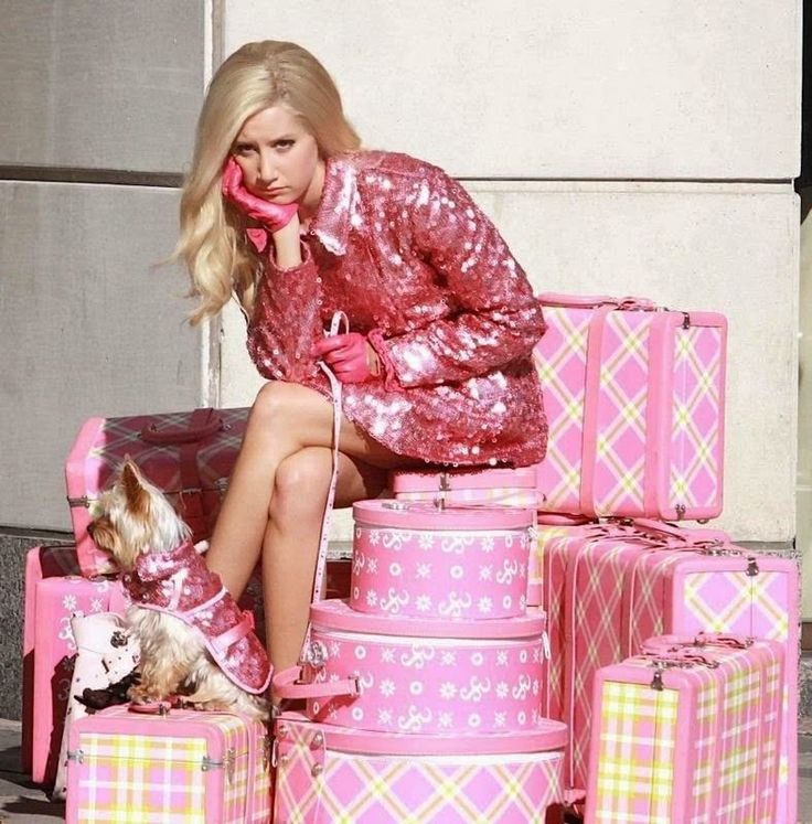 a woman sitting on top of pink suitcases next to a small dog and talking on the phone