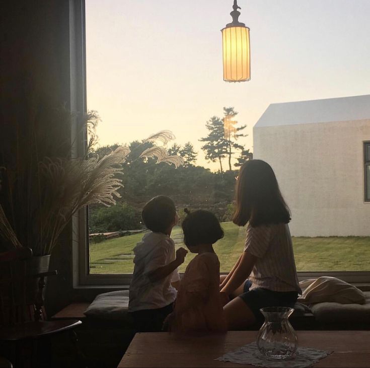 three children are sitting on a couch looking out the window at the grass and trees