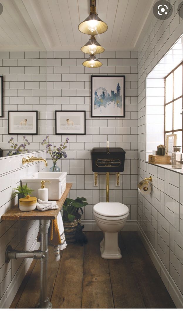 a bathroom with white tile walls and wood flooring is pictured in this image, there are pictures on the wall above the toilet