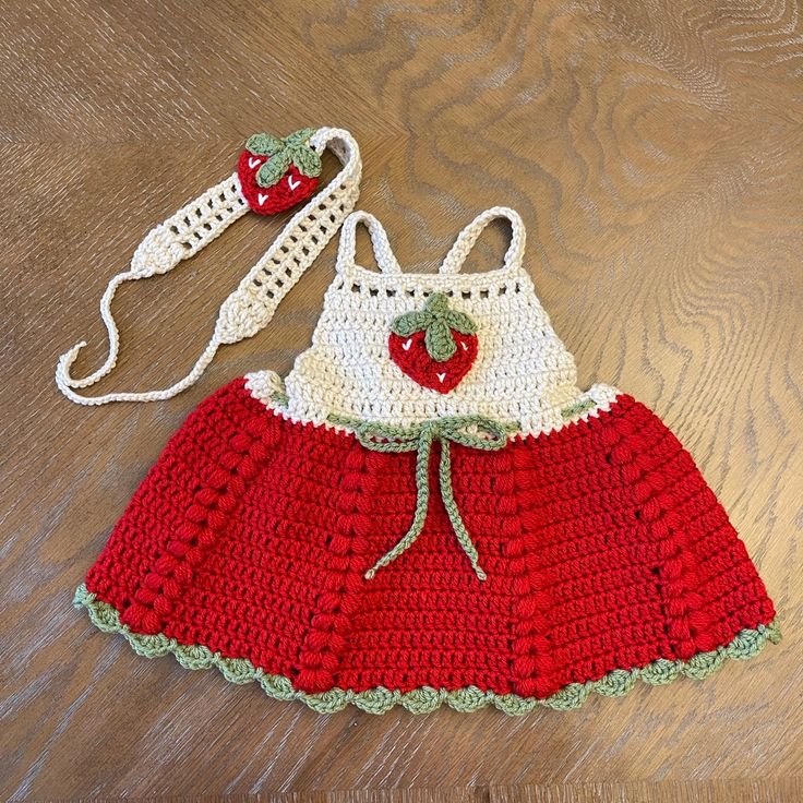 a crocheted red and white dress with strawberries on the back, sitting on a wooden surface